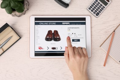 Woman with tablet shopping online at white wooden table, top view