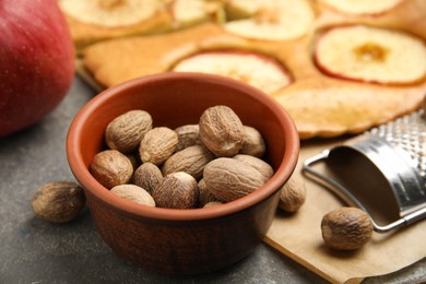 Photo of Nutmeg seeds, grater and apple pie on grey table, closeup