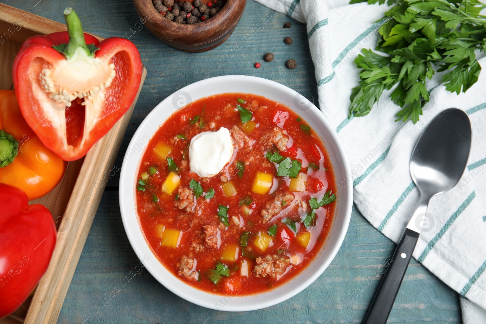 Photo of Bowl of delicious stuffed pepper soup on light blue wooden table, flat lay