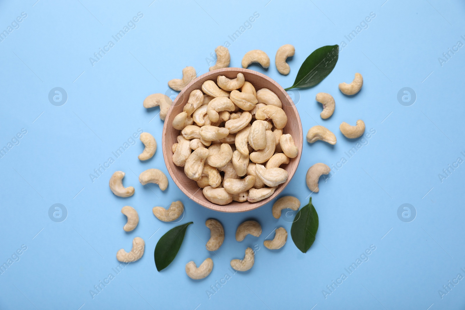 Photo of Many tasty cashew nuts and leaves on light blue background, top view