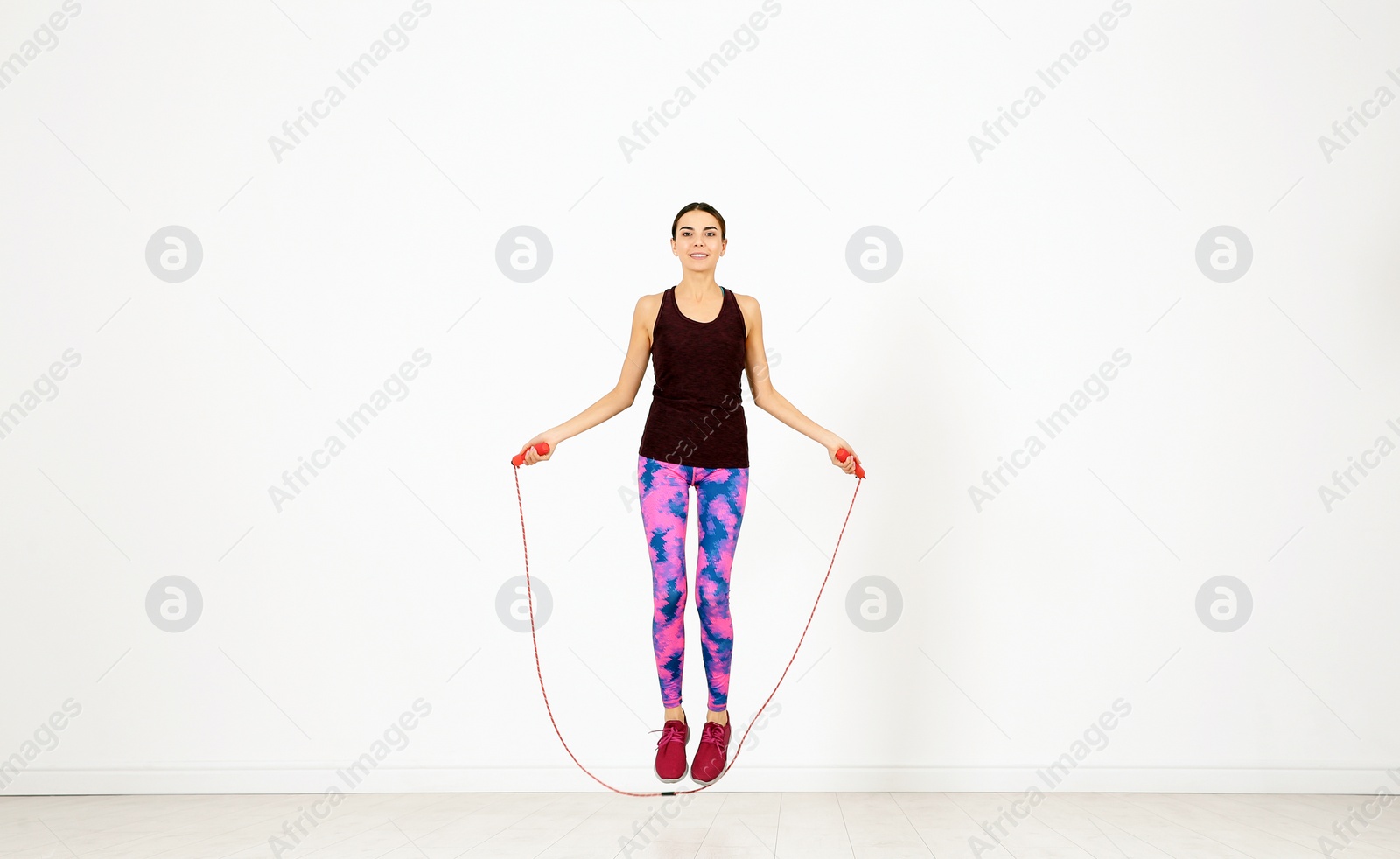 Photo of Full length portrait of young sportive woman training with jump rope in light room