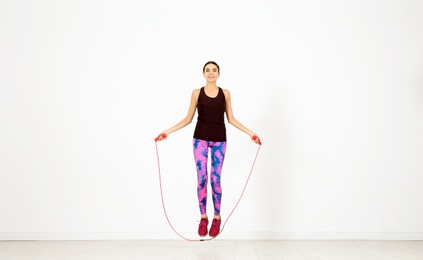 Full length portrait of young sportive woman training with jump rope in light room