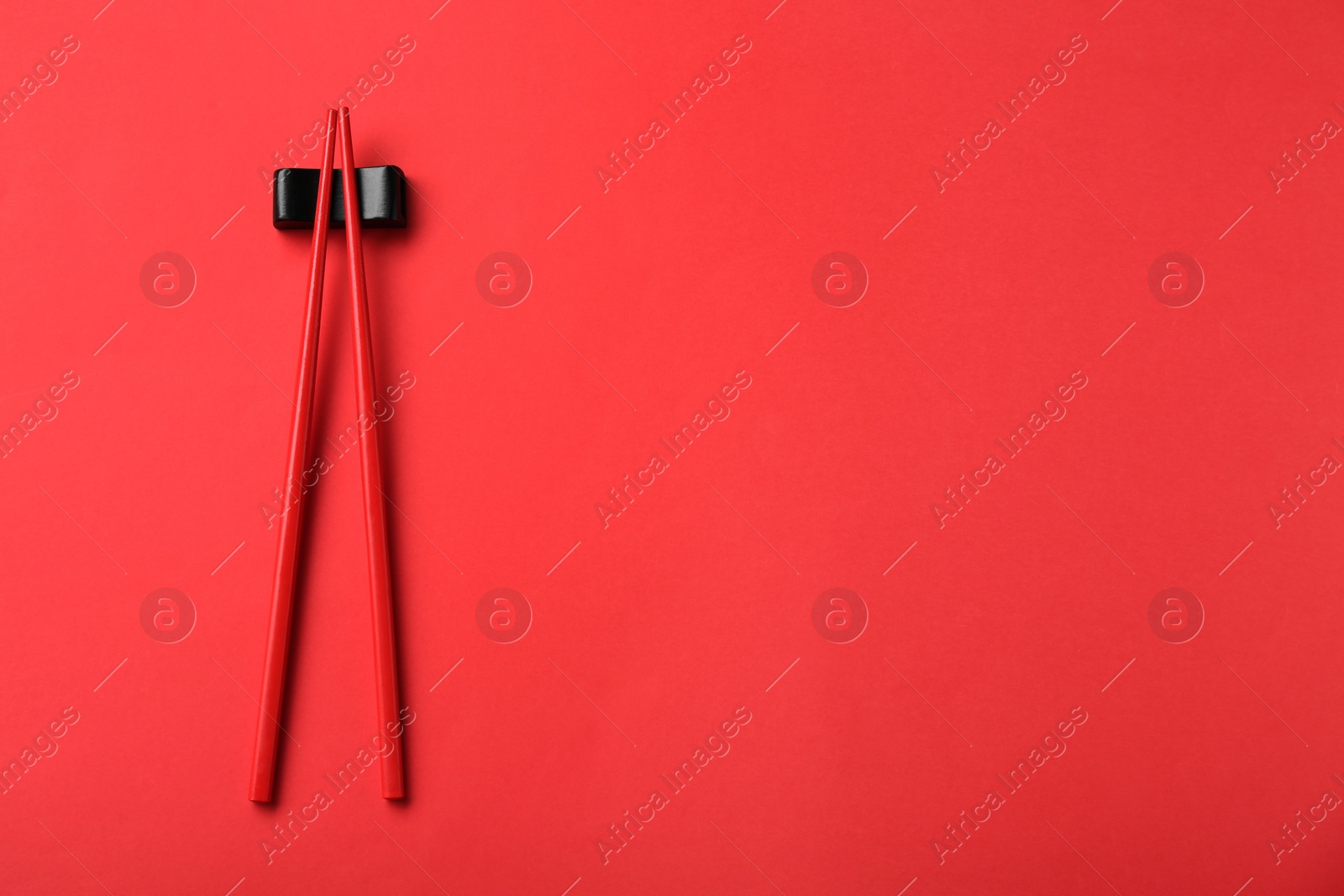 Photo of Pair of chopsticks with rest on red background, top view. Space for text