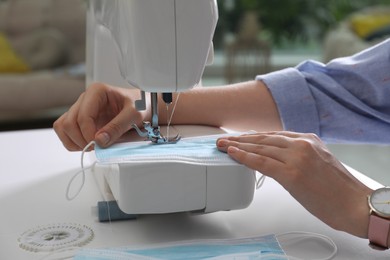 Photo of Woman sewing disposable protective mask with machine at table indoors, closeup