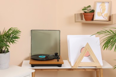 Photo of Stylish turntable with vinyl record on wooden table in cozy room