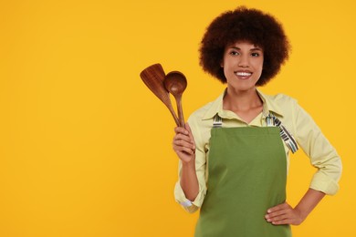 Photo of Happy young woman in apron holding spoon and spatula on orange background. Space for text