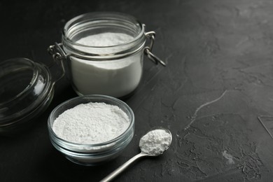 Photo of Baking powder in bowl, jar and spoon on black textured table, closeup. Space for text