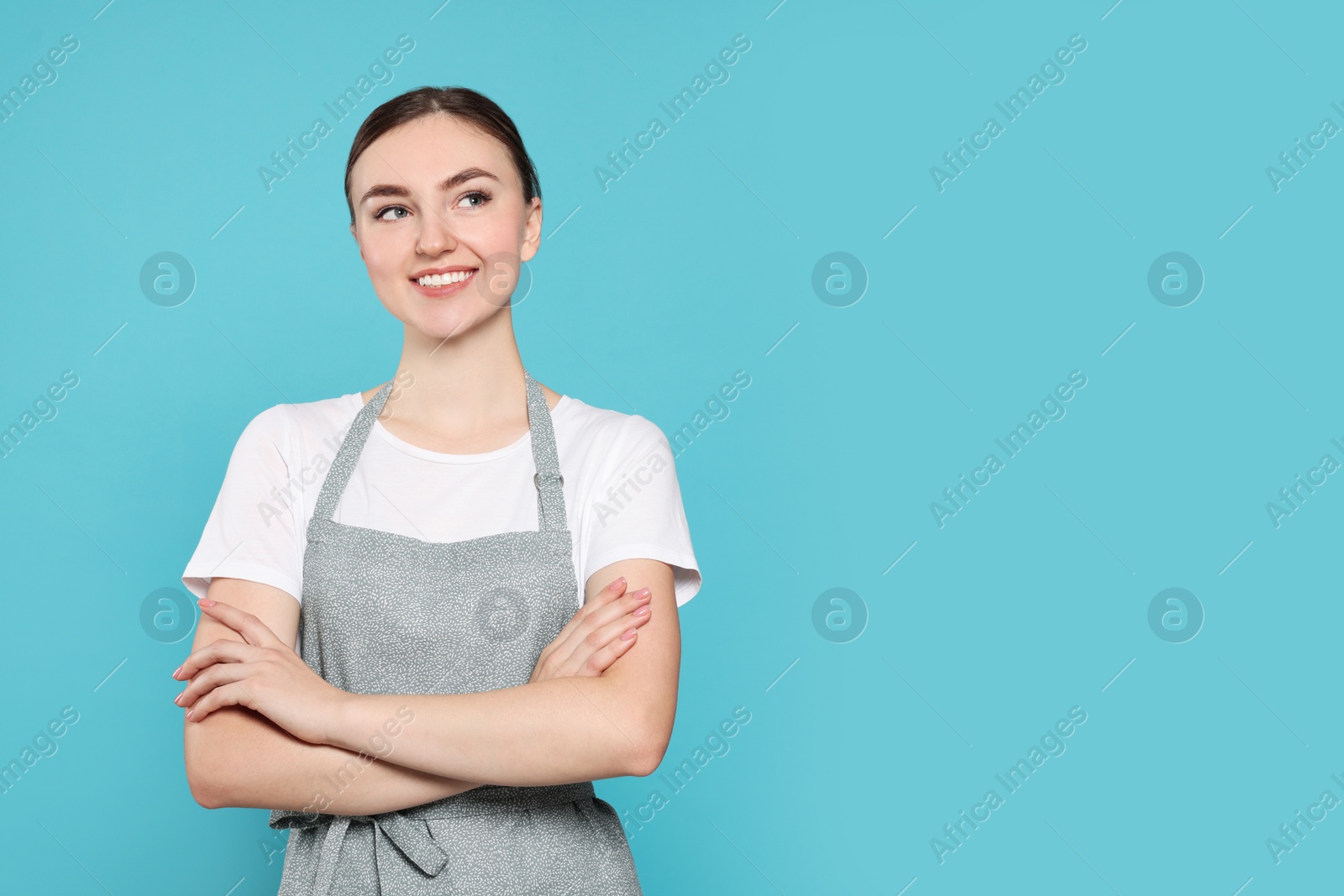 Photo of Beautiful young woman in clean apron with pattern on light blue background. Space for text