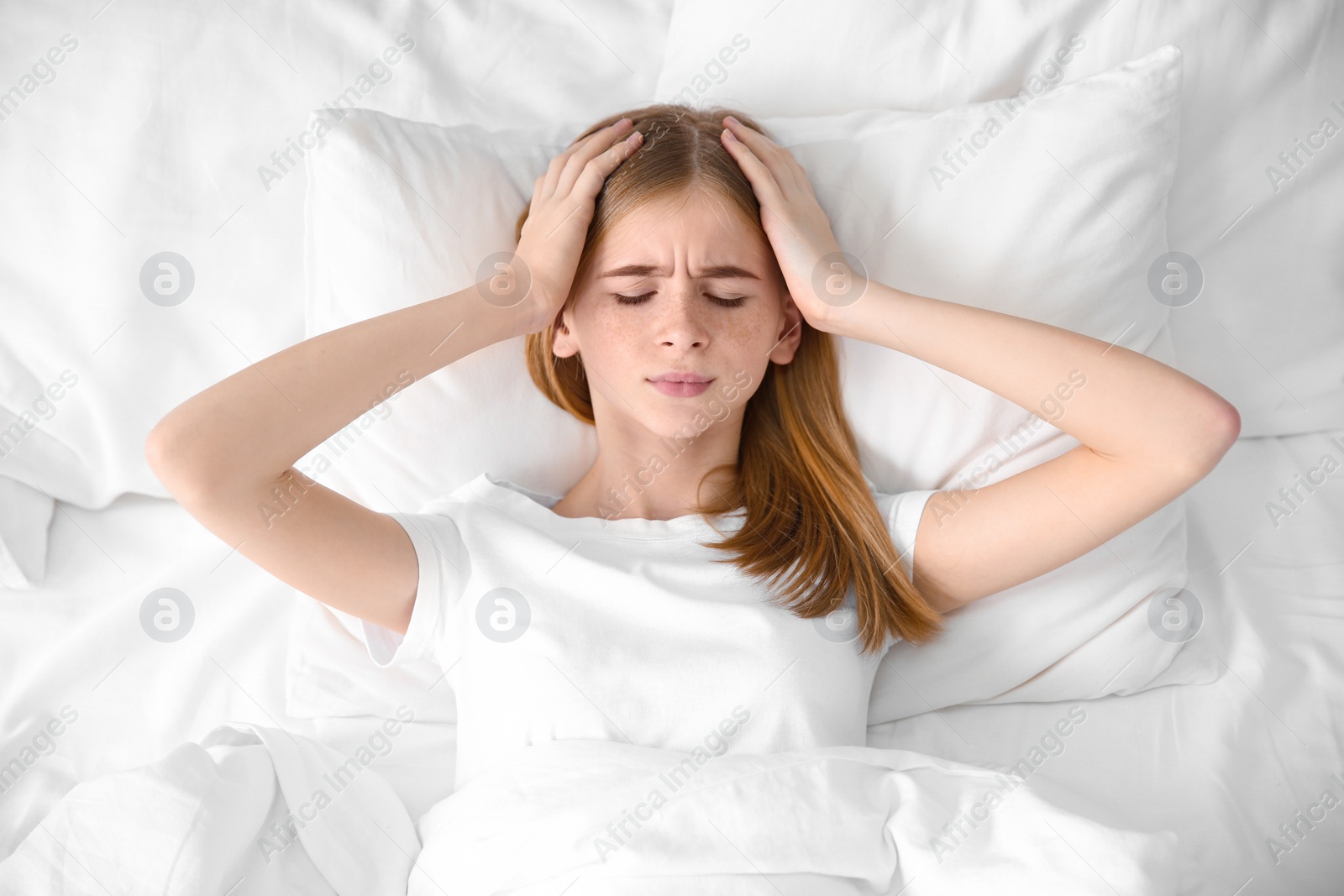 Photo of Teenage girl suffering from headache while lying in bed at home