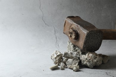 Photo of One sledgehammer and pieces of broken stones on grey background, closeup. Space for text