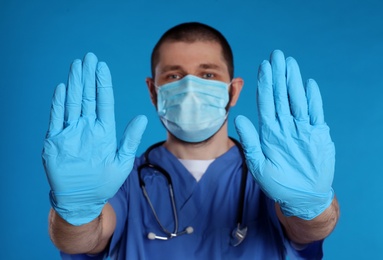 Doctor in protective mask showing stop gesture on light blue background. Prevent spreading of coronavirus