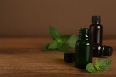 Photo of Glass bottles of nettle oil and leaves on wooden table against brown background, space for text