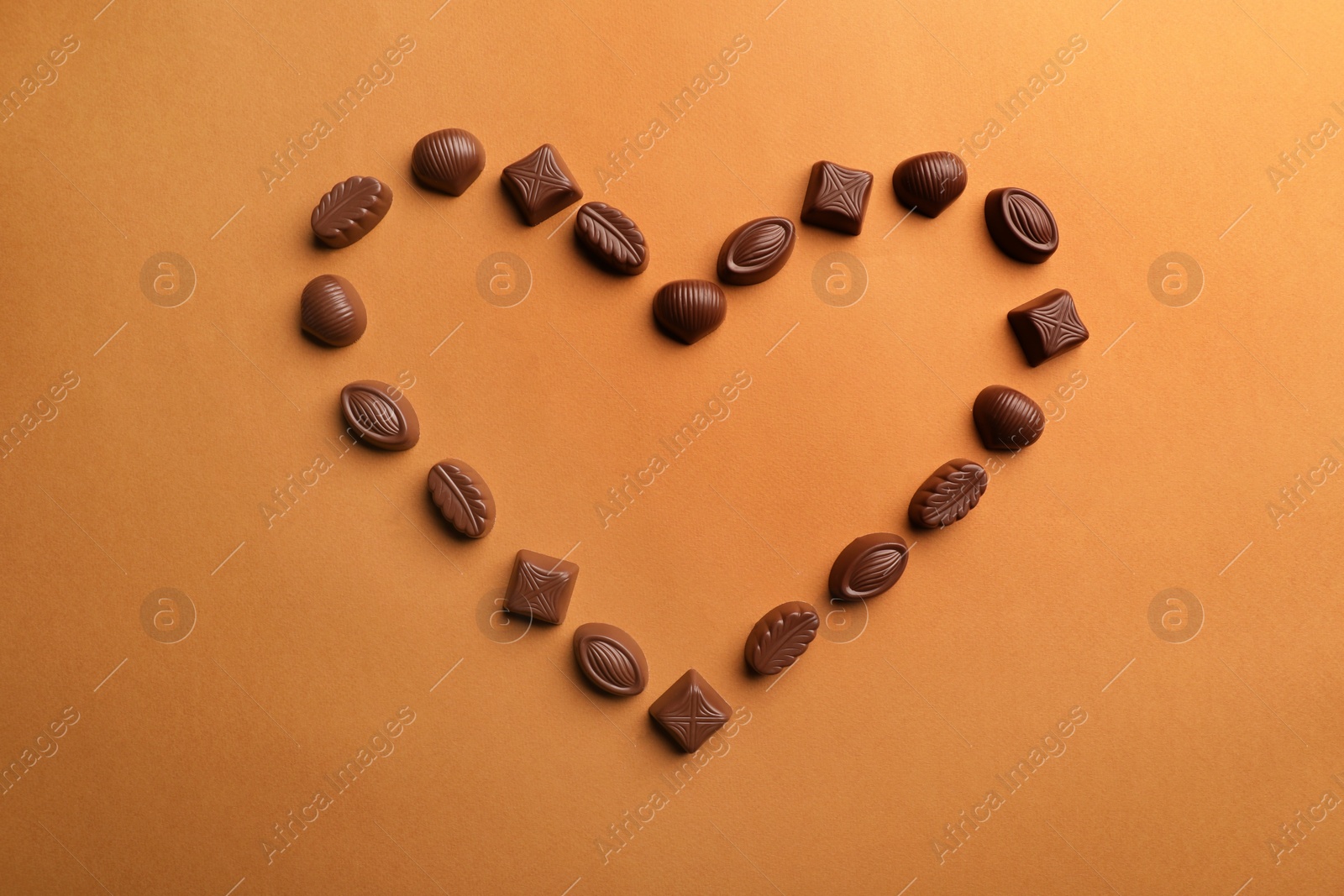 Photo of Heart made with delicious chocolate candies on brown background, top view