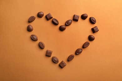 Photo of Heart made with delicious chocolate candies on brown background, top view