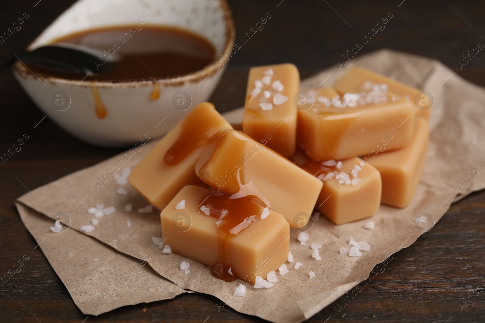 Photo of Delicious candies with sea salt and caramel sauce on wooden table, closeup