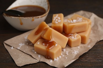 Delicious candies with sea salt and caramel sauce on wooden table, closeup