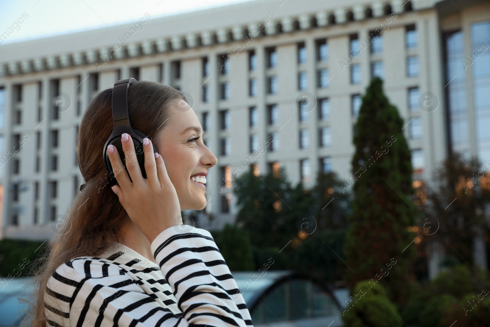 Photo of Happy woman in headphones listening to music on city street. Space for text