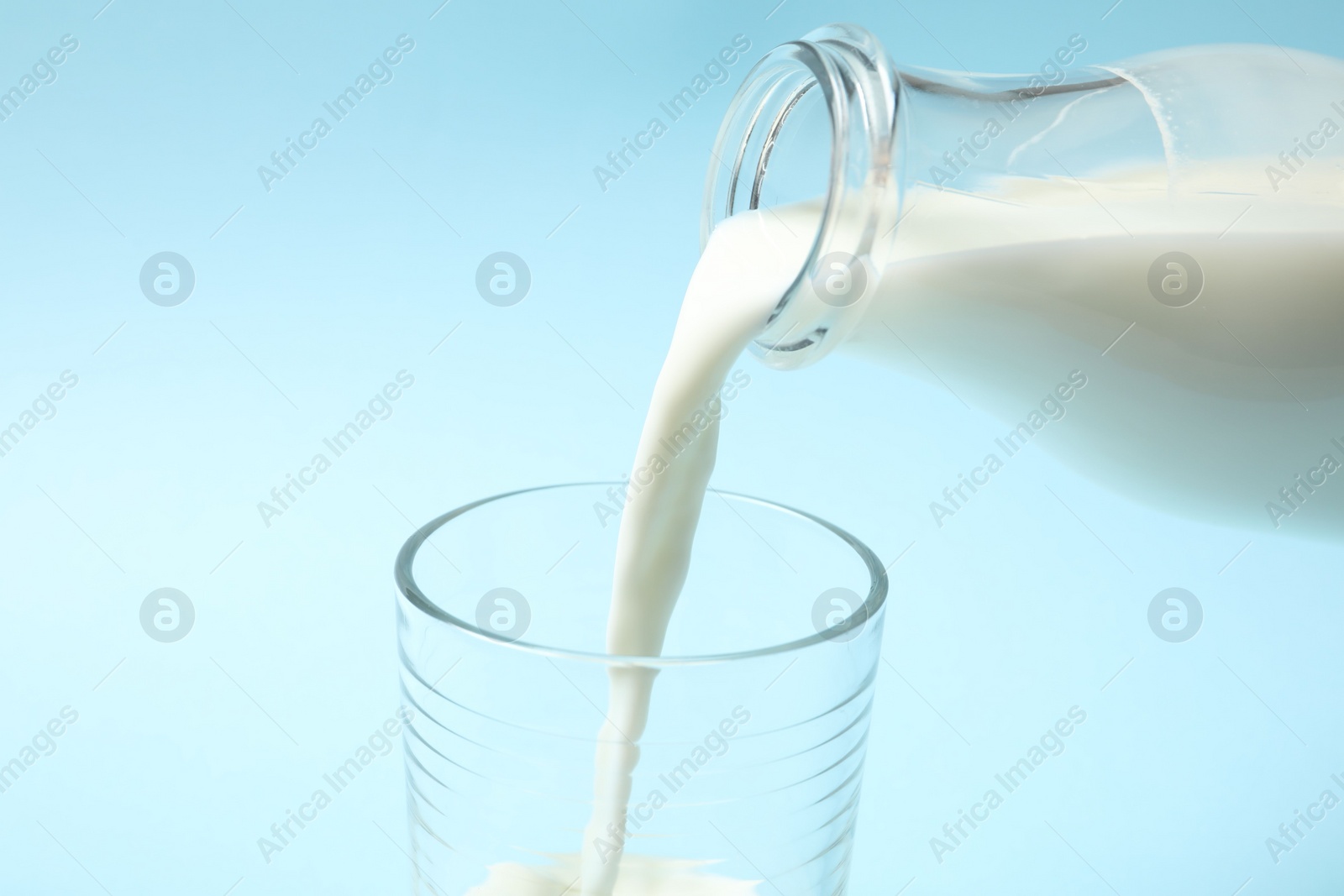 Photo of Pouring milk into glass on light blue background, closeup