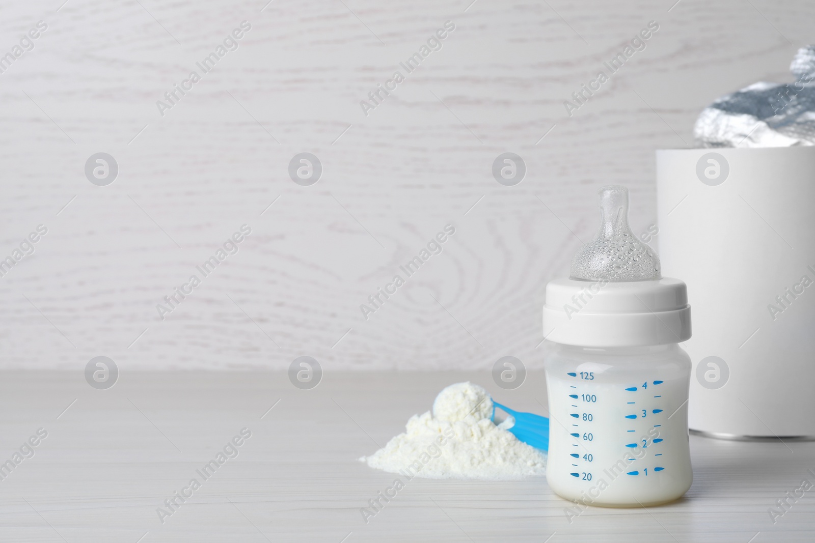 Photo of Powdered infant formula, scoop and feeding bottle on white wooden table, space for text. Baby milk