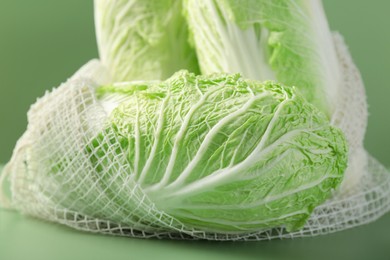 Fresh Chinese cabbages in string bag on green background, closeup