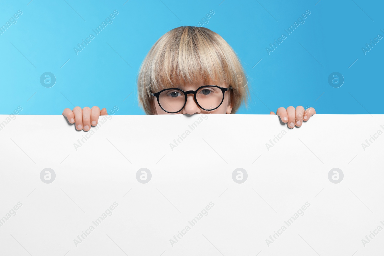 Photo of Cute little boy in glasses with blank board on light blue background