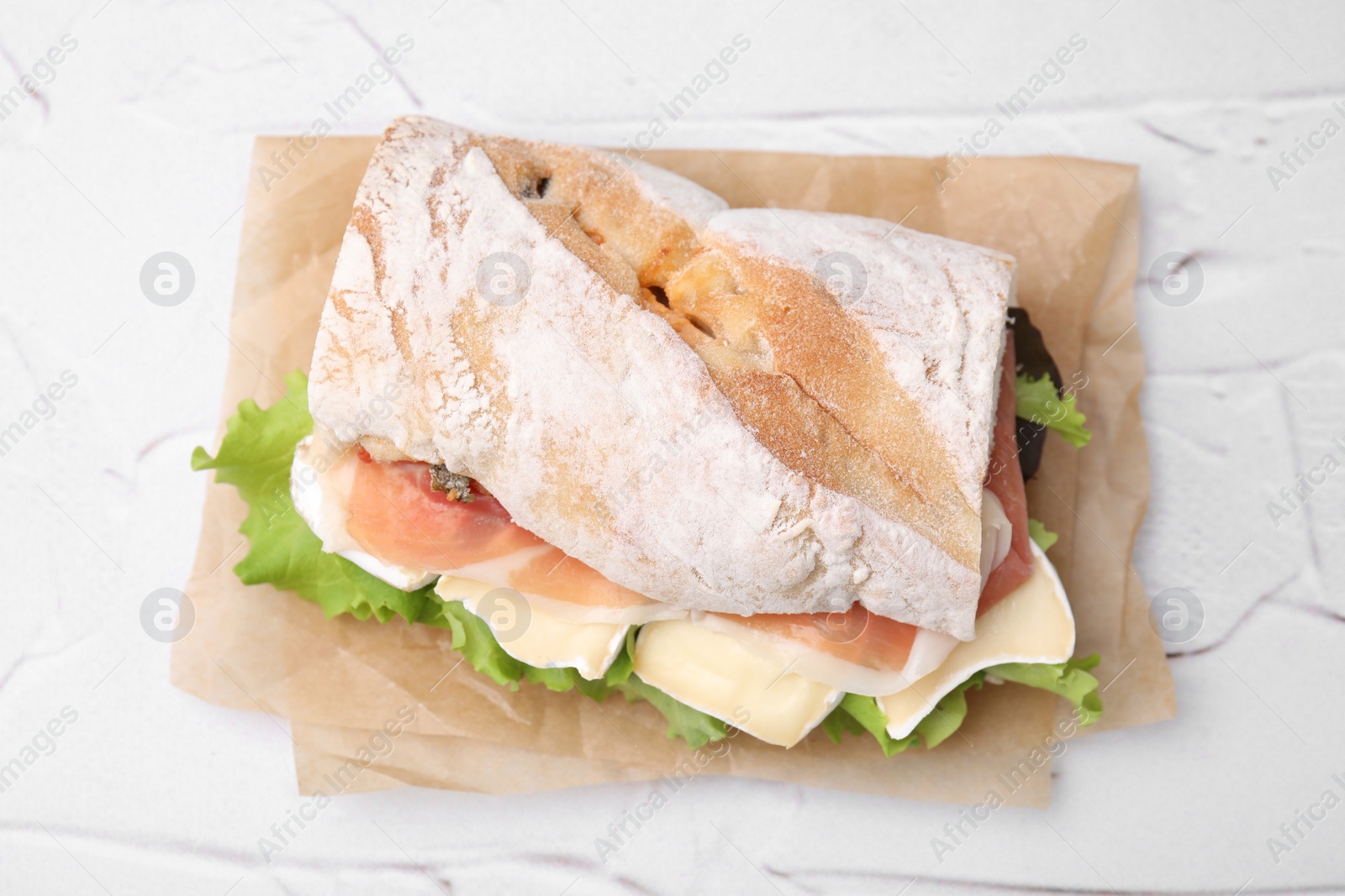 Photo of Tasty sandwich with brie cheese and prosciutto on white textured table, top view