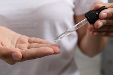 Photo of Woman applying cosmetic serum onto her finger on blurred background, closeup