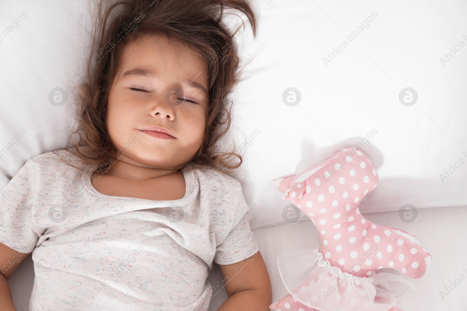 Photo of Cute little girl with toy sleeping on bed, view from above