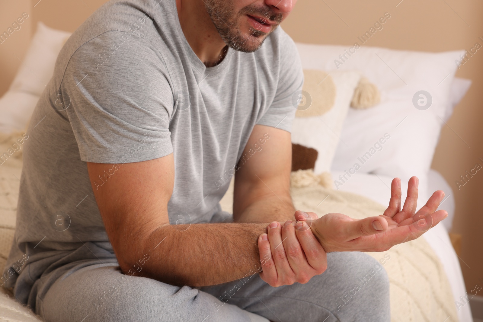 Photo of Man suffering from pain in his hand on bed indoors, closeup