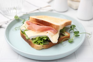 Photo of Tasty sandwich with brie cheese and prosciutto on white tiled table, closeup