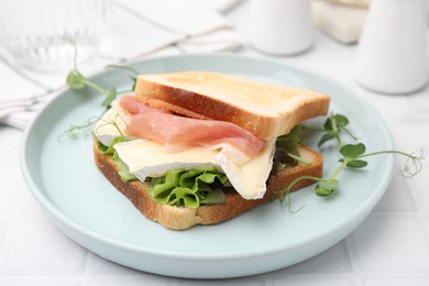 Tasty sandwich with brie cheese and prosciutto on white tiled table, closeup