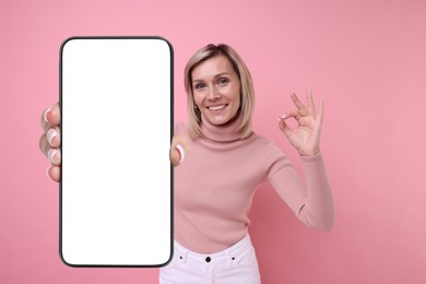 Image of Happy woman showing mobile phone with blank screen on pink background. Mockup for design