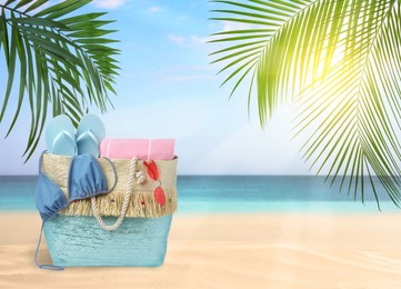 Image of Stylish bag with different accessories on tropical sandy beach, space for text 