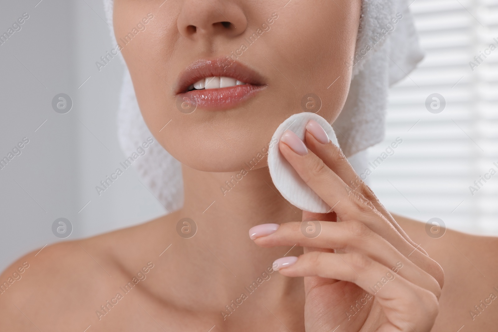 Photo of Young woman cleaning her face with cotton pad indoors, closeup