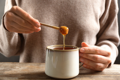 Photo of Woman putting honey into tea at wooden table, closeup