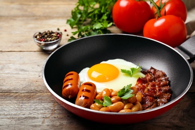 Frying pan with traditional English breakfast on wooden table