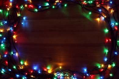 Photo of Frame of colorful Christmas lights on wooden table, top view. Space for text