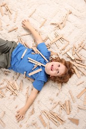 Cute little boy surrounded by wooden construction set on carpet at home, top view. Child`s toy