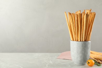 Photo of Delicious grissini sticks, rosemary and tomato on grey marble table. Space for text