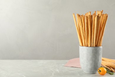 Delicious grissini sticks, rosemary and tomato on grey marble table. Space for text