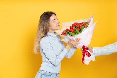 Happy woman receiving red tulip bouquet from man on yellow background. 8th of March celebration