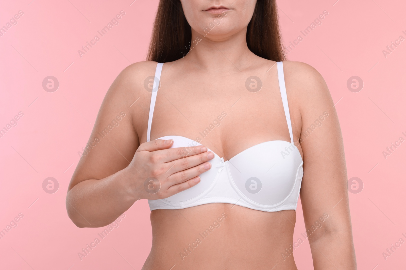 Photo of Mammology. Woman in bra doing breast self-examination on pink background, closeup