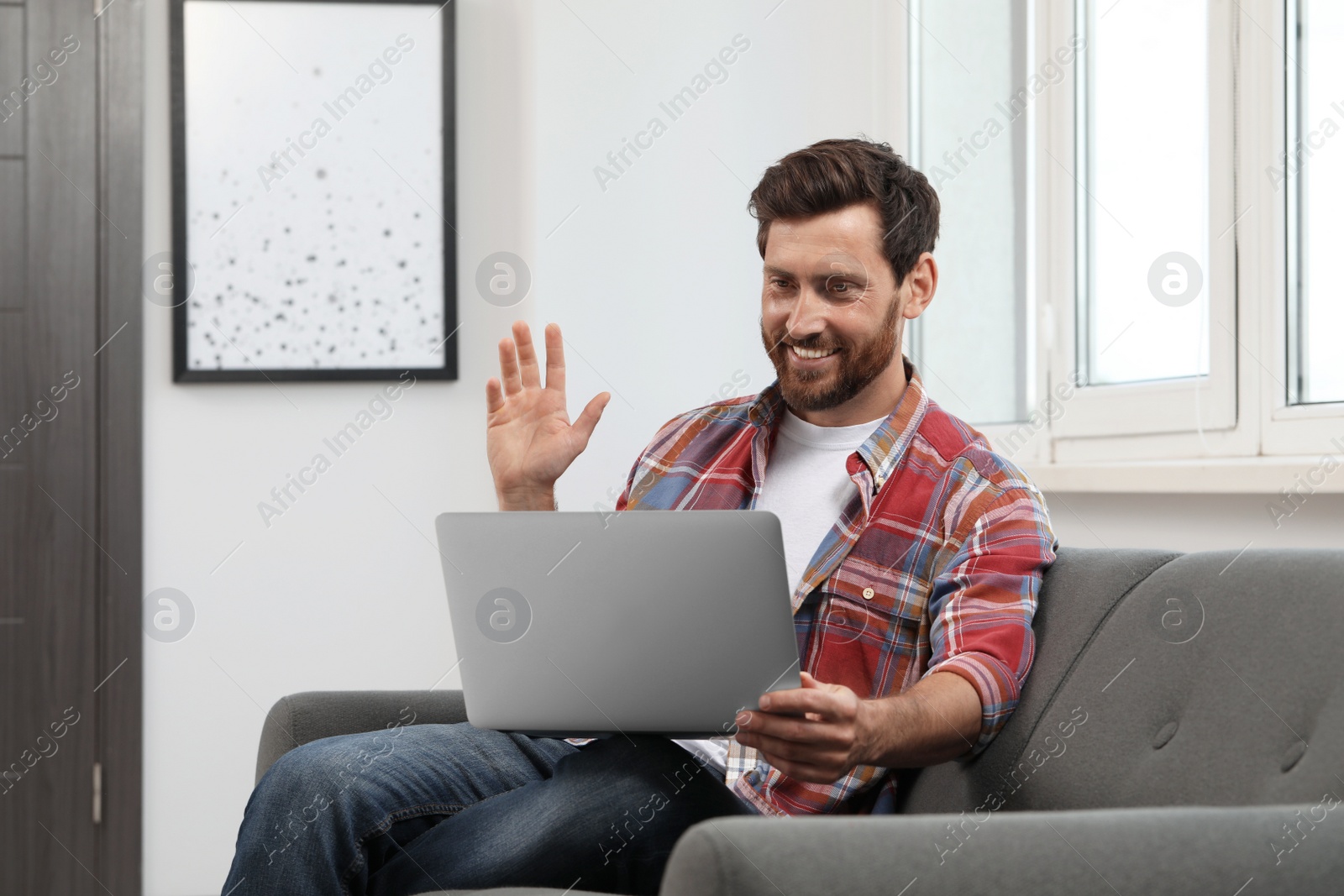 Photo of Happy bearded man having video chat on laptop at home
