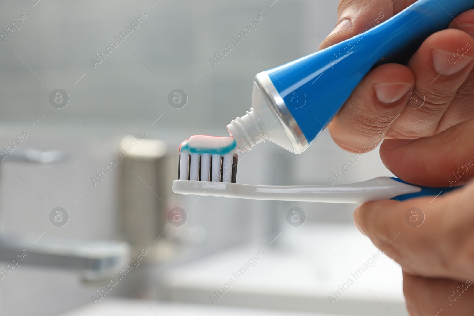 Photo of Man applying toothpaste on brush in bathroom, closeup