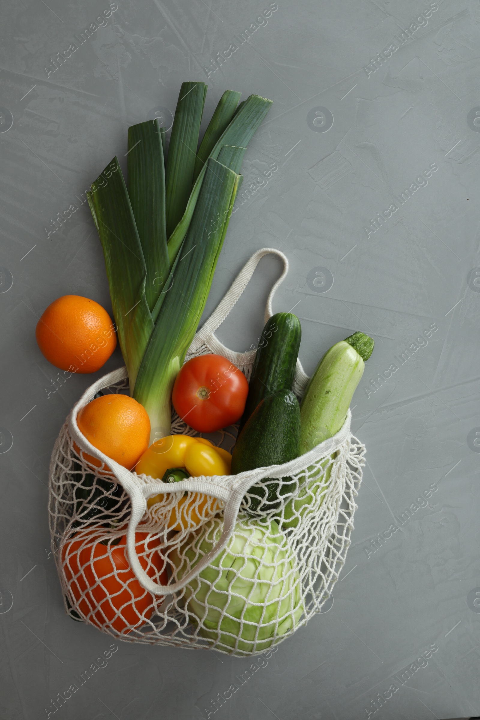 Photo of Net bag with fruits and vegetables on light grey table, flat lay