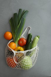 Photo of Net bag with fruits and vegetables on light grey table, flat lay