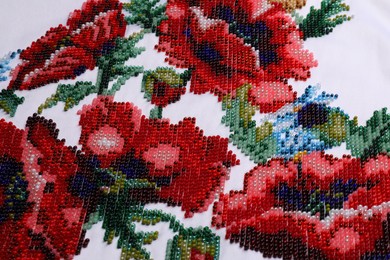 Photo of Beautiful floral bead embroidery on white fabric, closeup