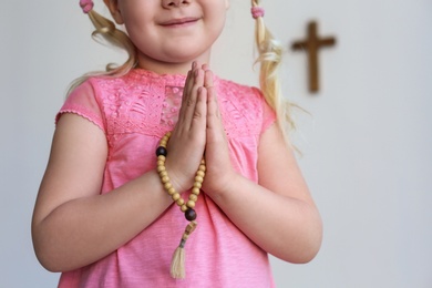 Photo of Little girl with beads praying near light wall