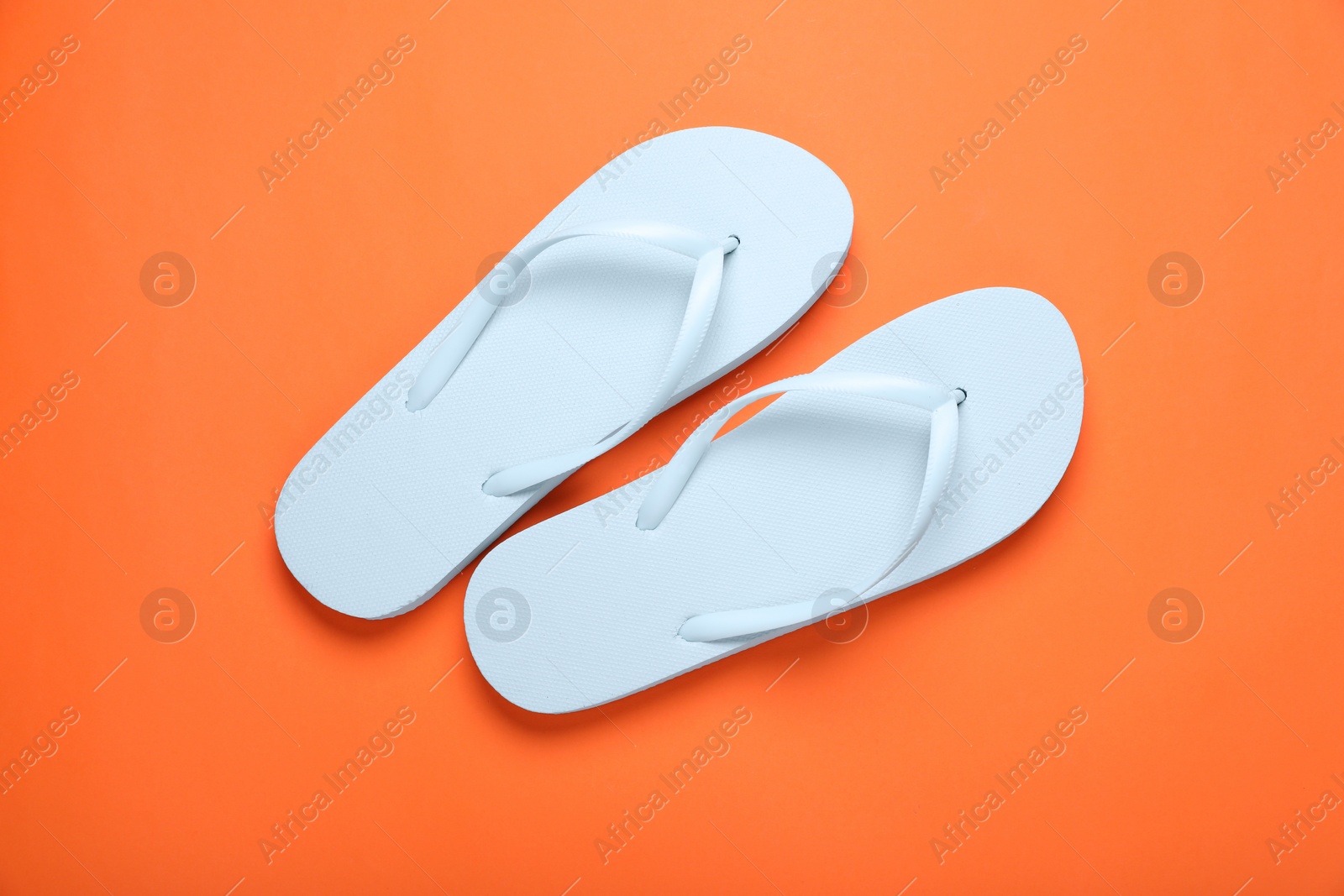 Photo of Stylish white flip flops on orange background, top view