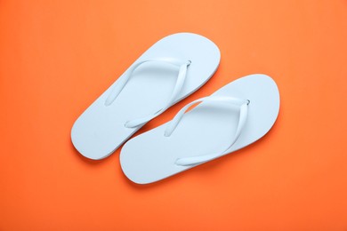 Stylish white flip flops on orange background, top view